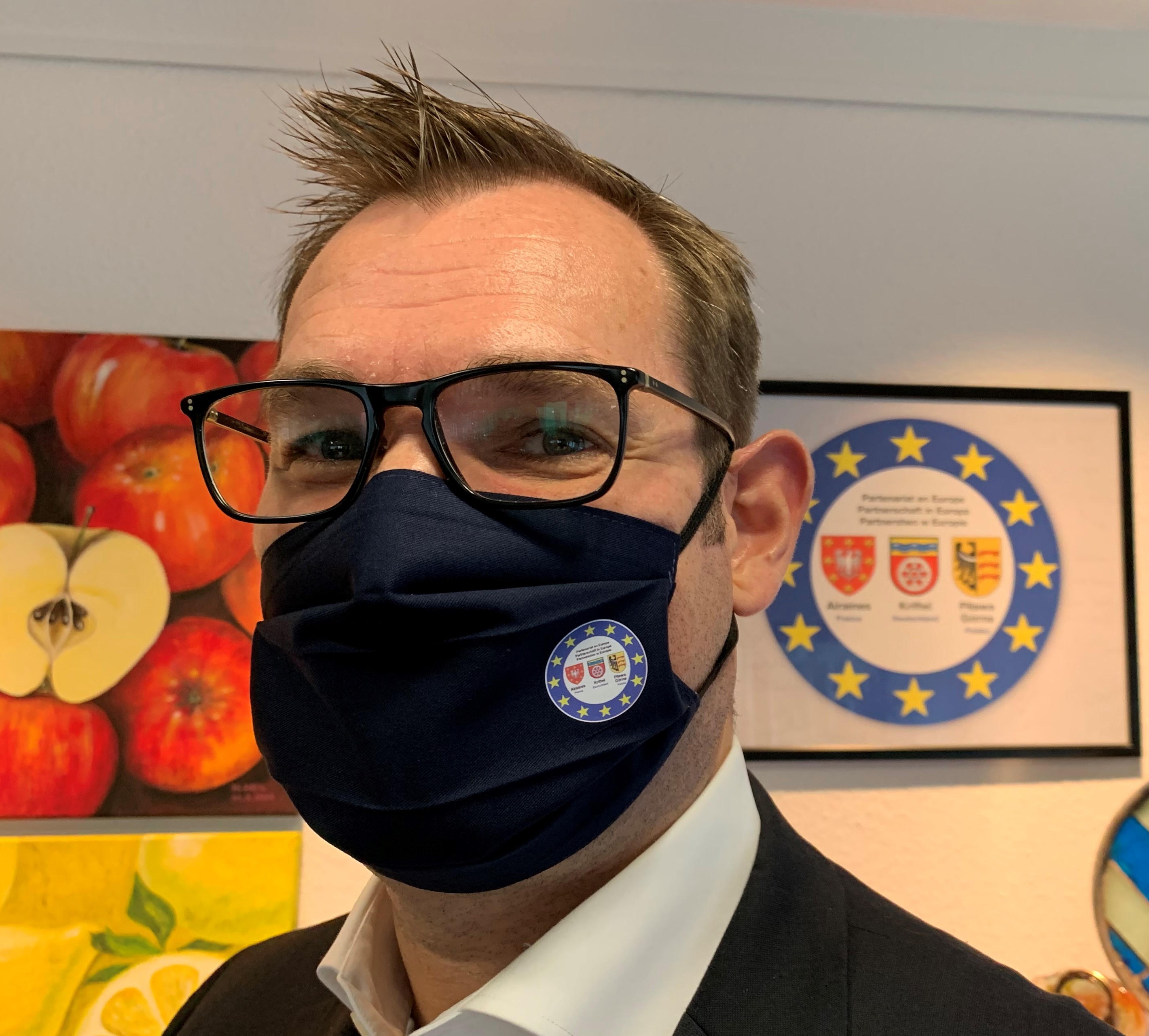 Bürgermeister Seitz trägt eine blaue Maske mit dem Logo der Partnerschaft Kriftel - Airaines - Pilawa Gorna.