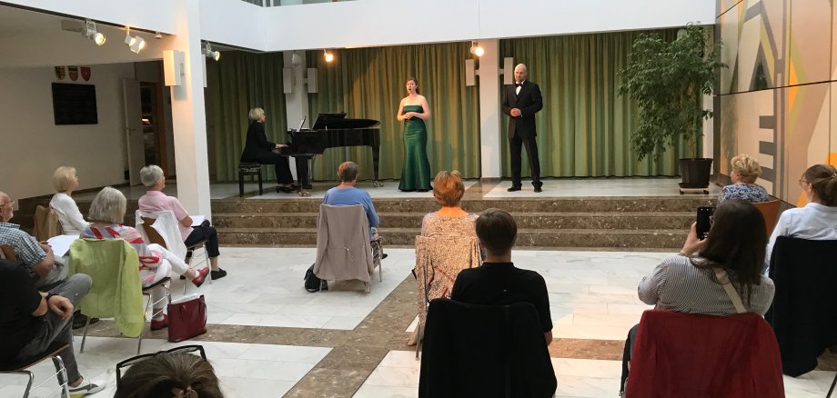 Zwei Sänger und eine Pianistin auf der Bühne, wenige Zuschauer auf weit entfernten Stühlen.