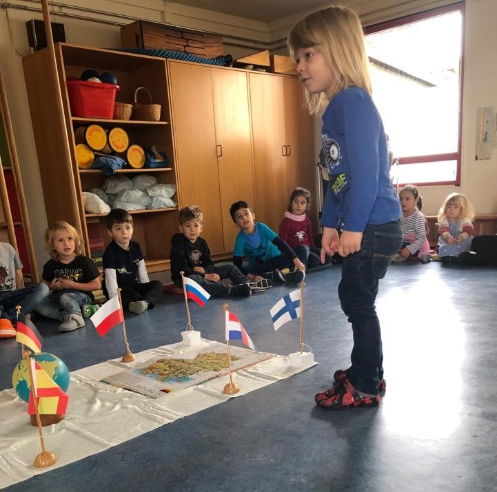 Kinder sitzen um eine Decke mit bunten Flaggen herum.