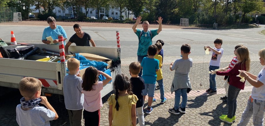 Mitarbeiter des bauhofes teilen an die Kinder Zangen, Säcke und Handschuhe aus.