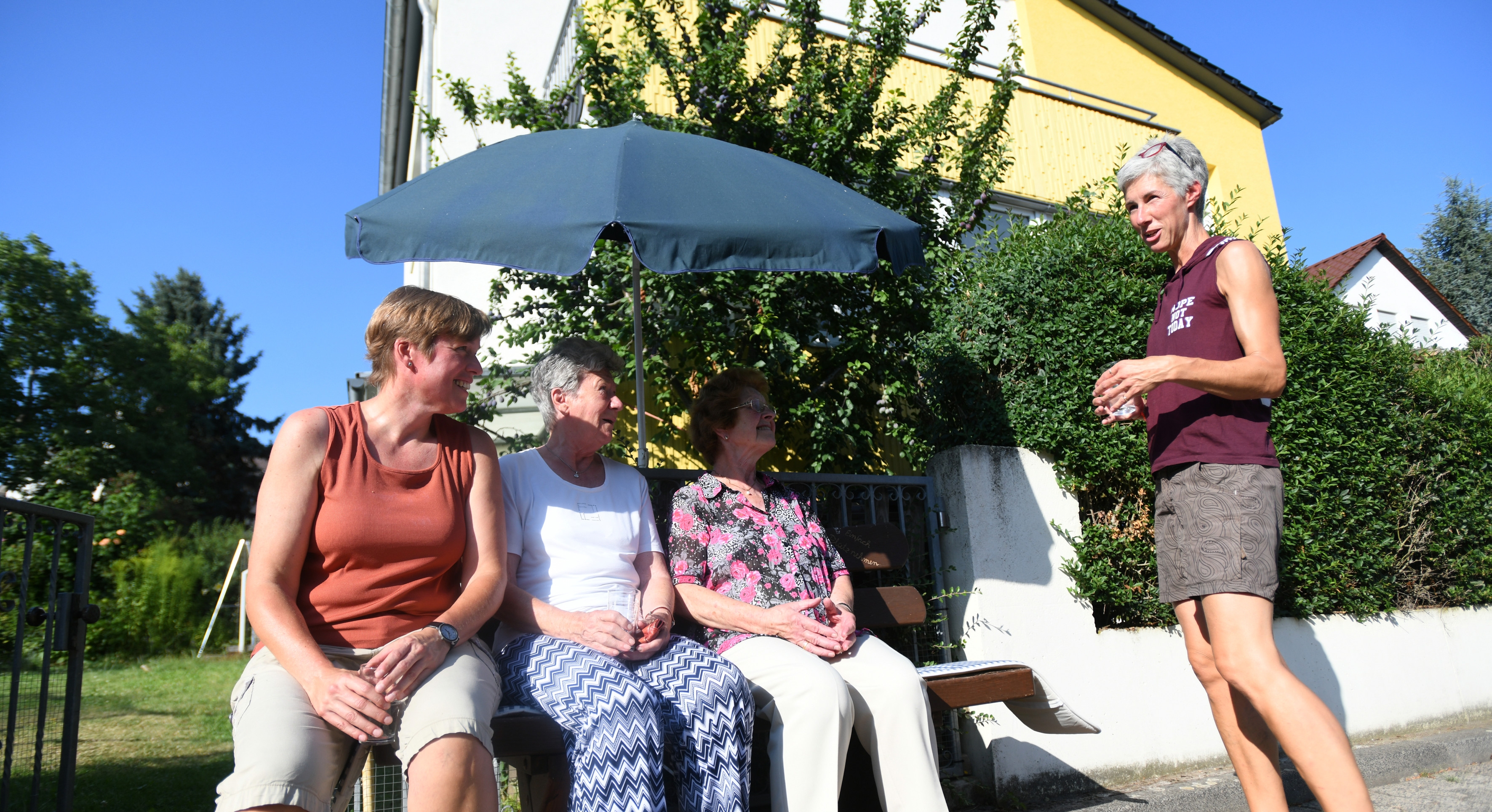 Nachbarinnen plauschen auf einer bank unter dem Sonnenschirm.