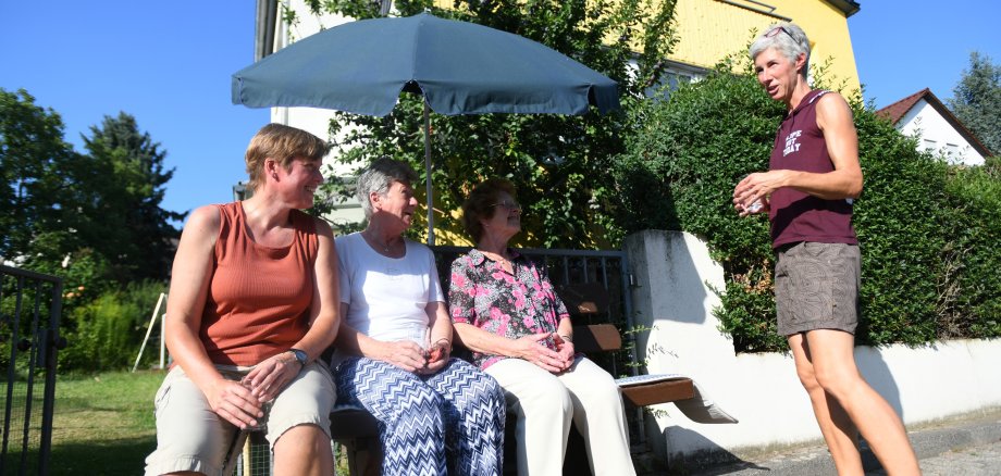 Nachbarinnen plauschen auf einer bank unter dem Sonnenschirm.