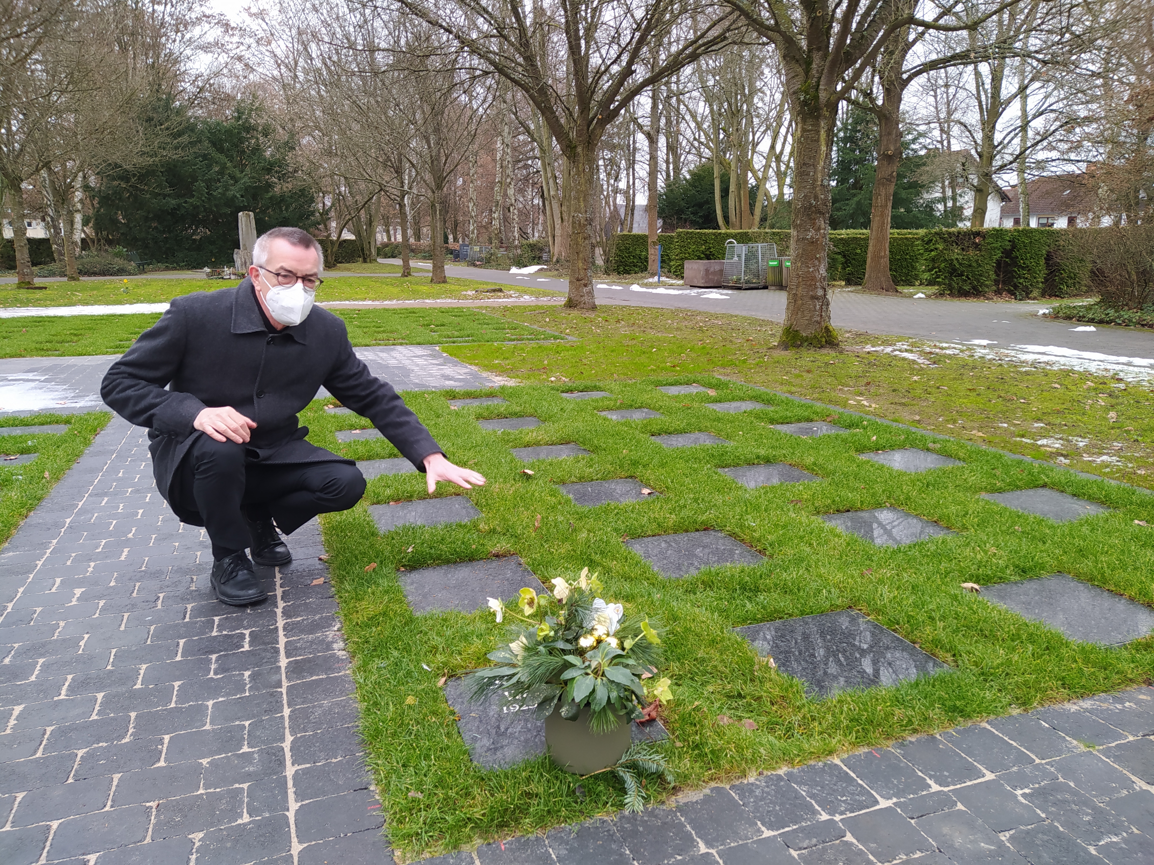 Franz Jirasek mit Maske kniet neben dem neuen Urnenrasenfeld.