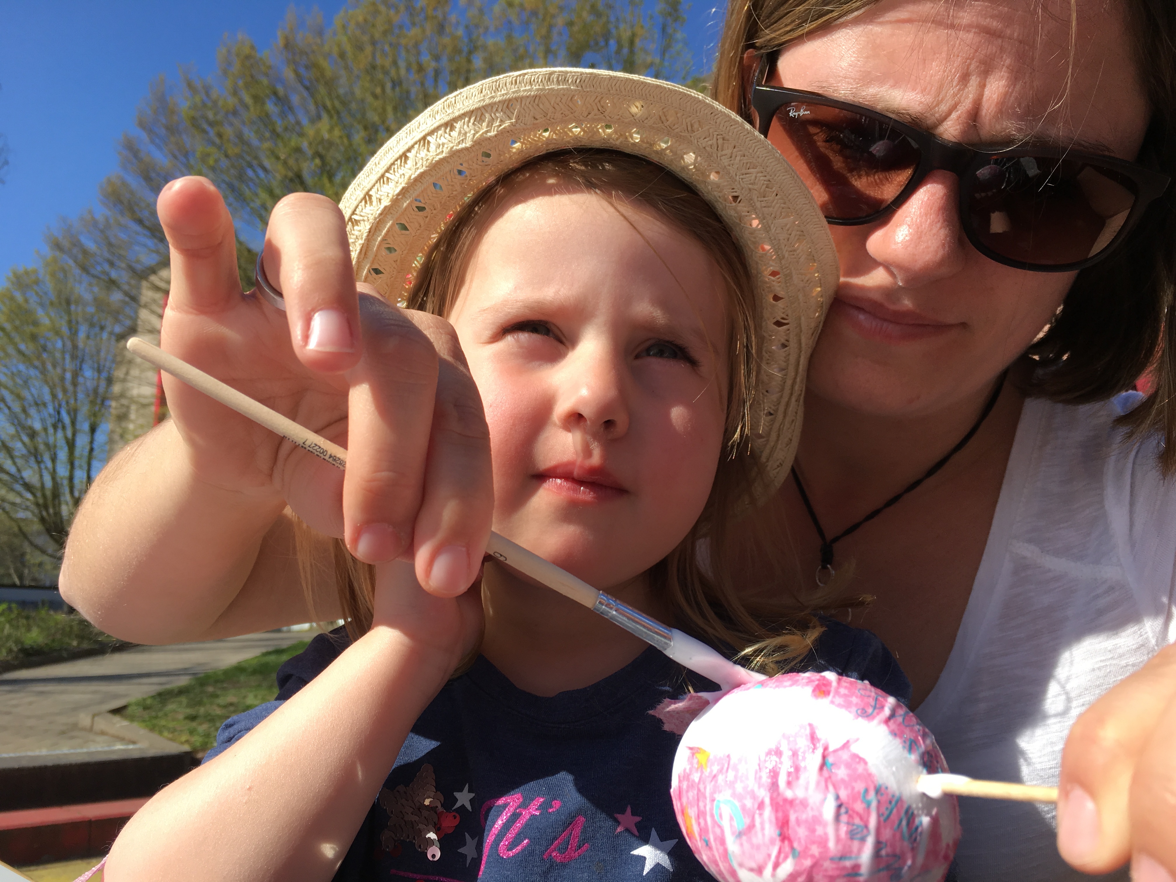 Ein KInd auf dem Schoß der Mutter bemalt ein Osterei.