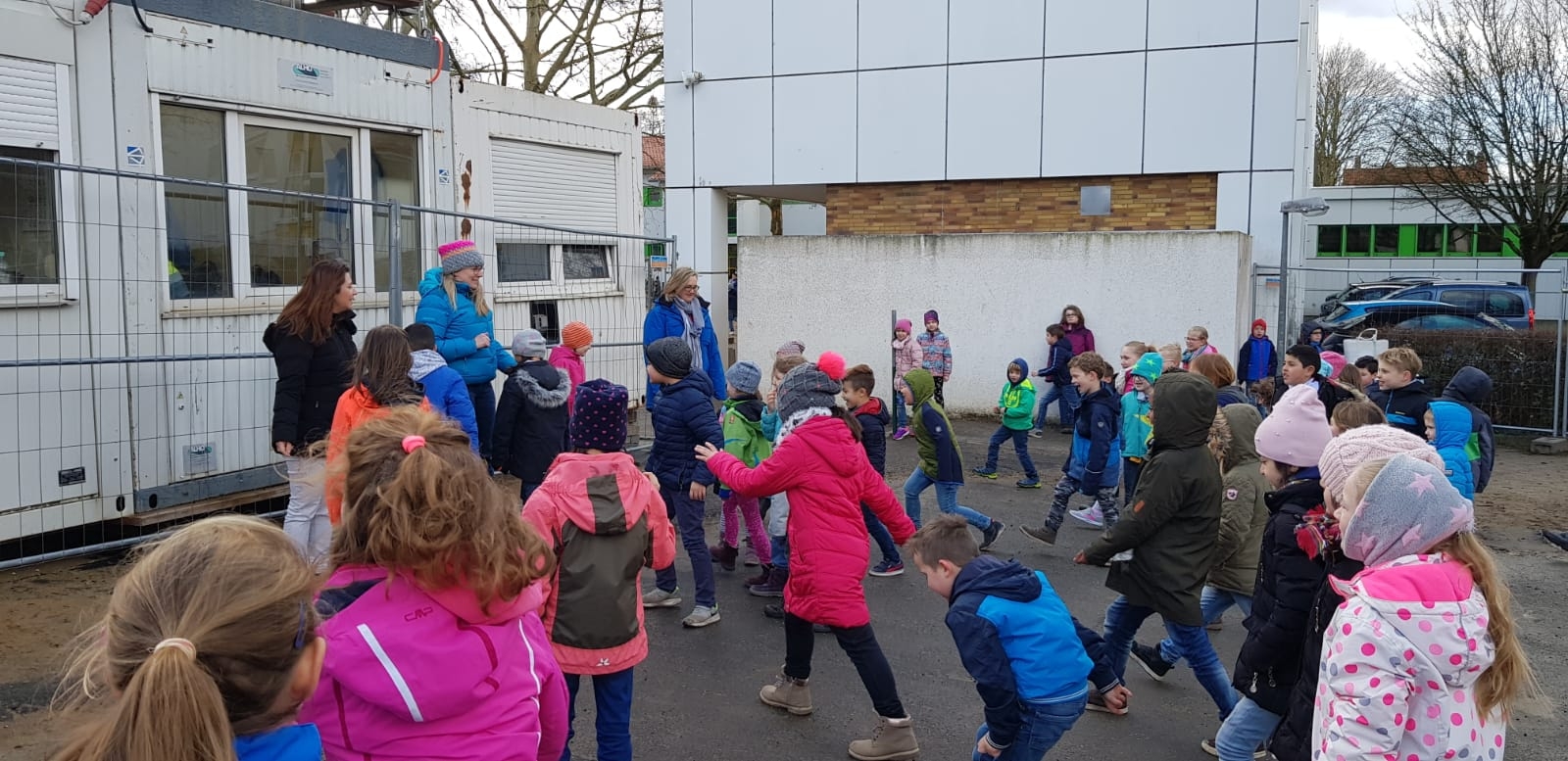 Kinder stehen um zwei Mütter herum auf dem Pausenhof.