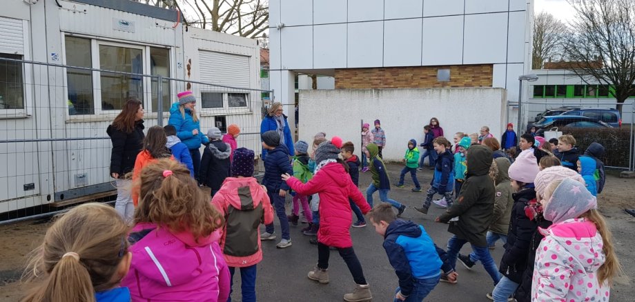 Kinder stehen um zwei Mütter herum auf dem Pausenhof.
