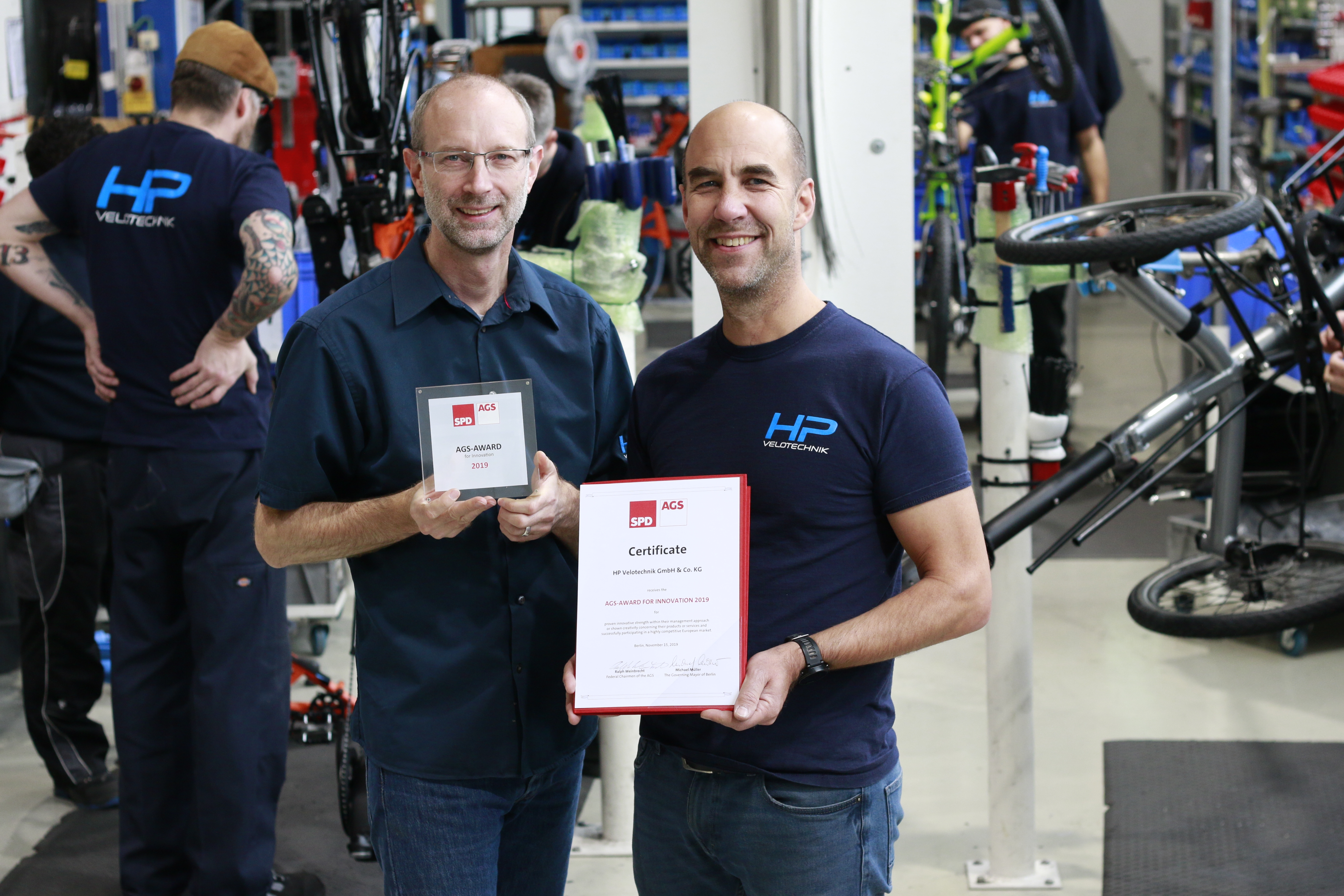 Die Geschäftsführer Pulvermüller und Hollants mit ihrem Preis in der Werkstatt von Velotechnik..