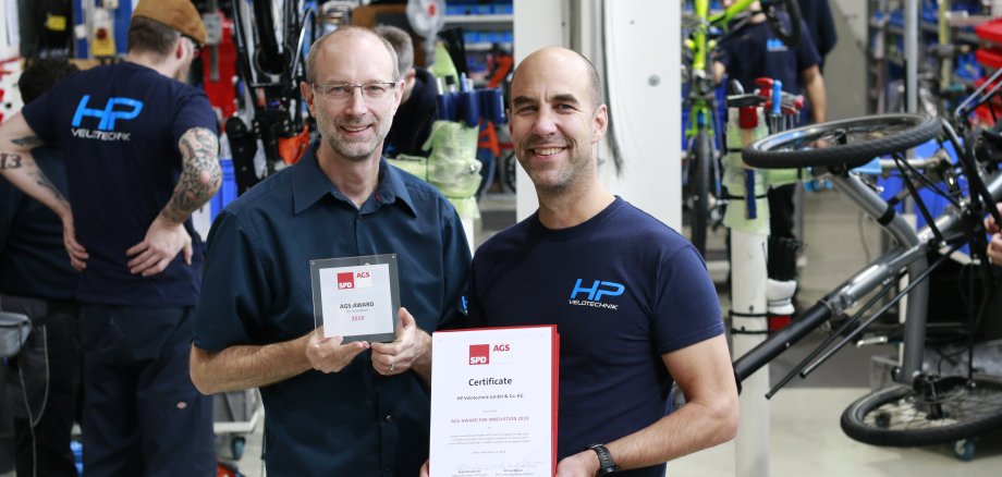 Die Geschäftsführer Pulvermüller und Hollants mit ihrem Preis in der Werkstatt von Velotechnik..