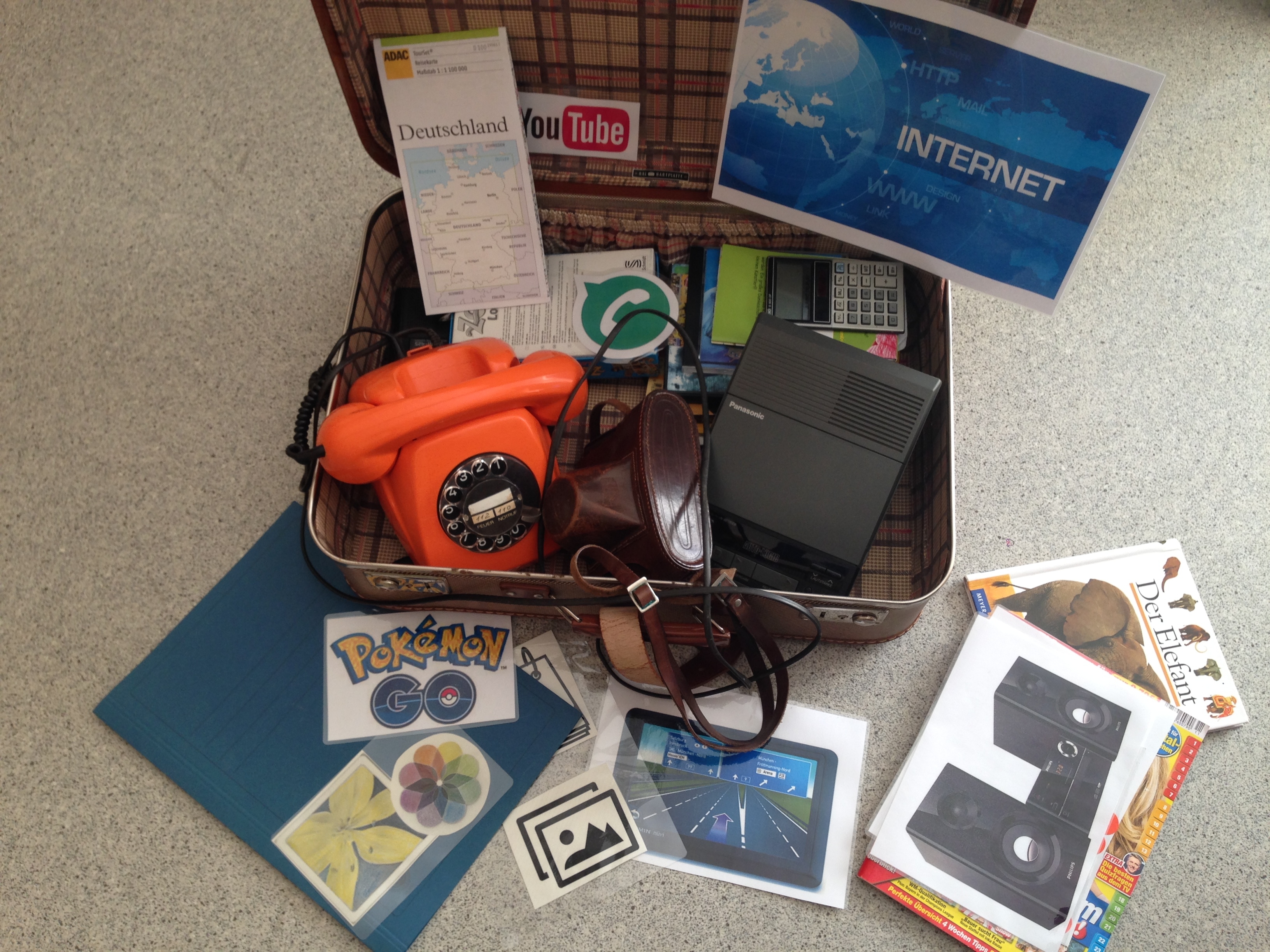 Ein altes Telefon und ein Kofferv voll Verlockungen, was man mit einem modernen Handy machen kann.