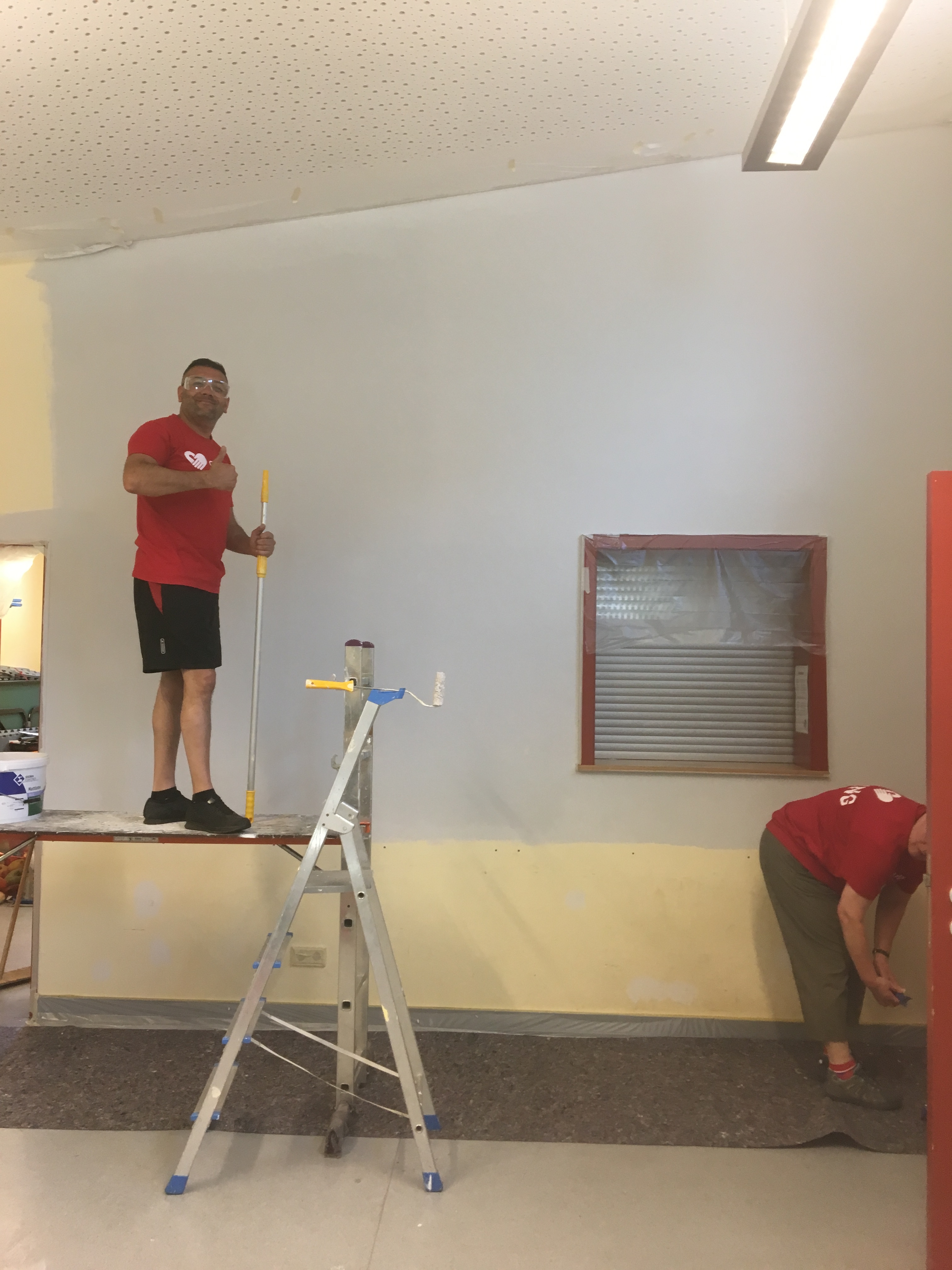 Ein Mann mit Pinsel steht auf einem Gerüst im Freizeithaus.