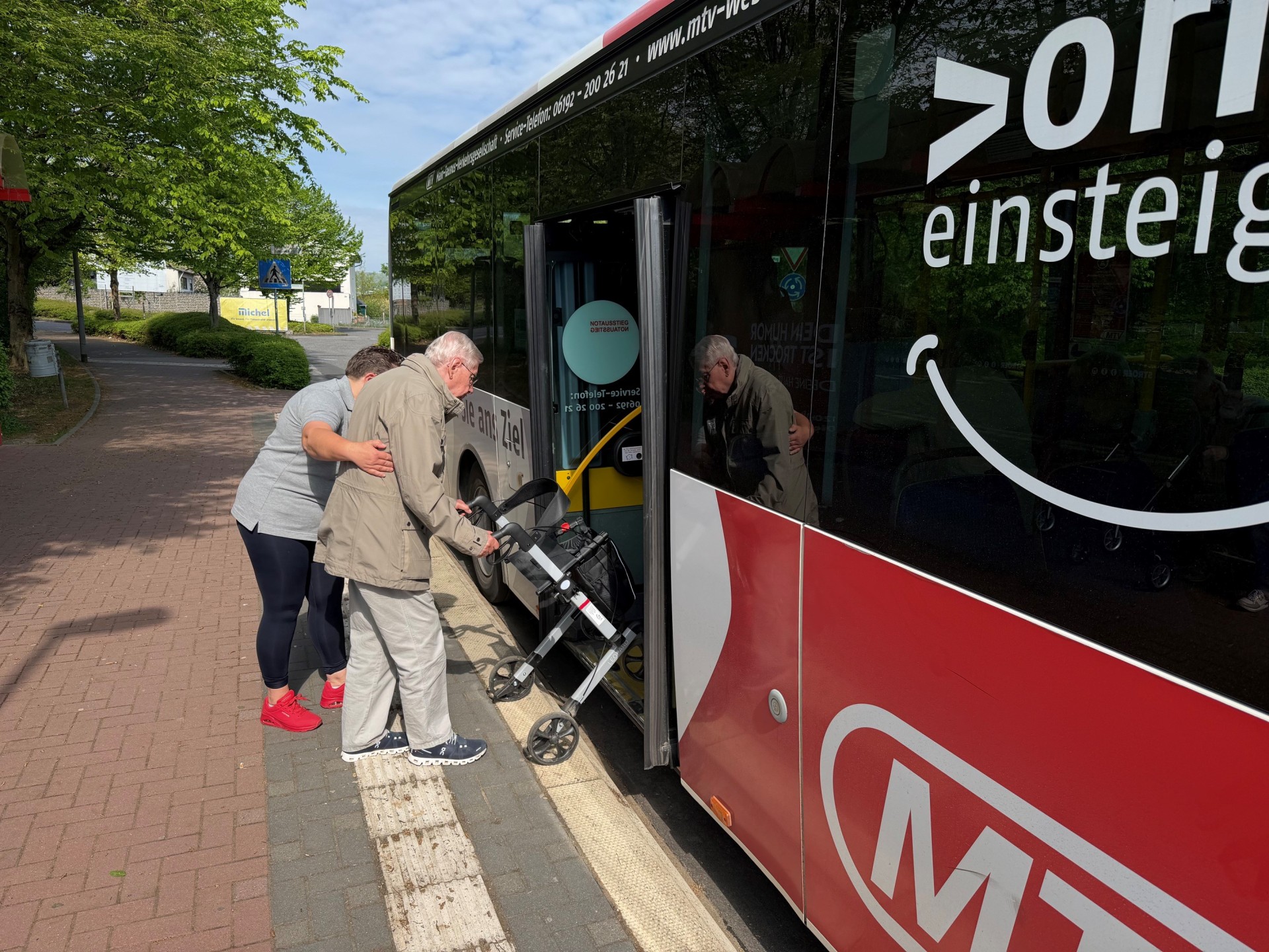 Eine Frau hilft einem Rollator-Fahrer in den Bus.
