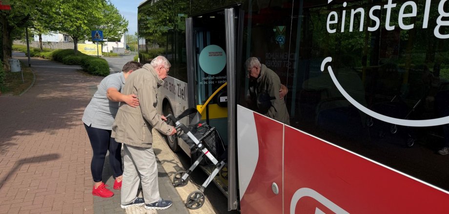Eine Frau hilft einem Rollator-Fahrer in den Bus.