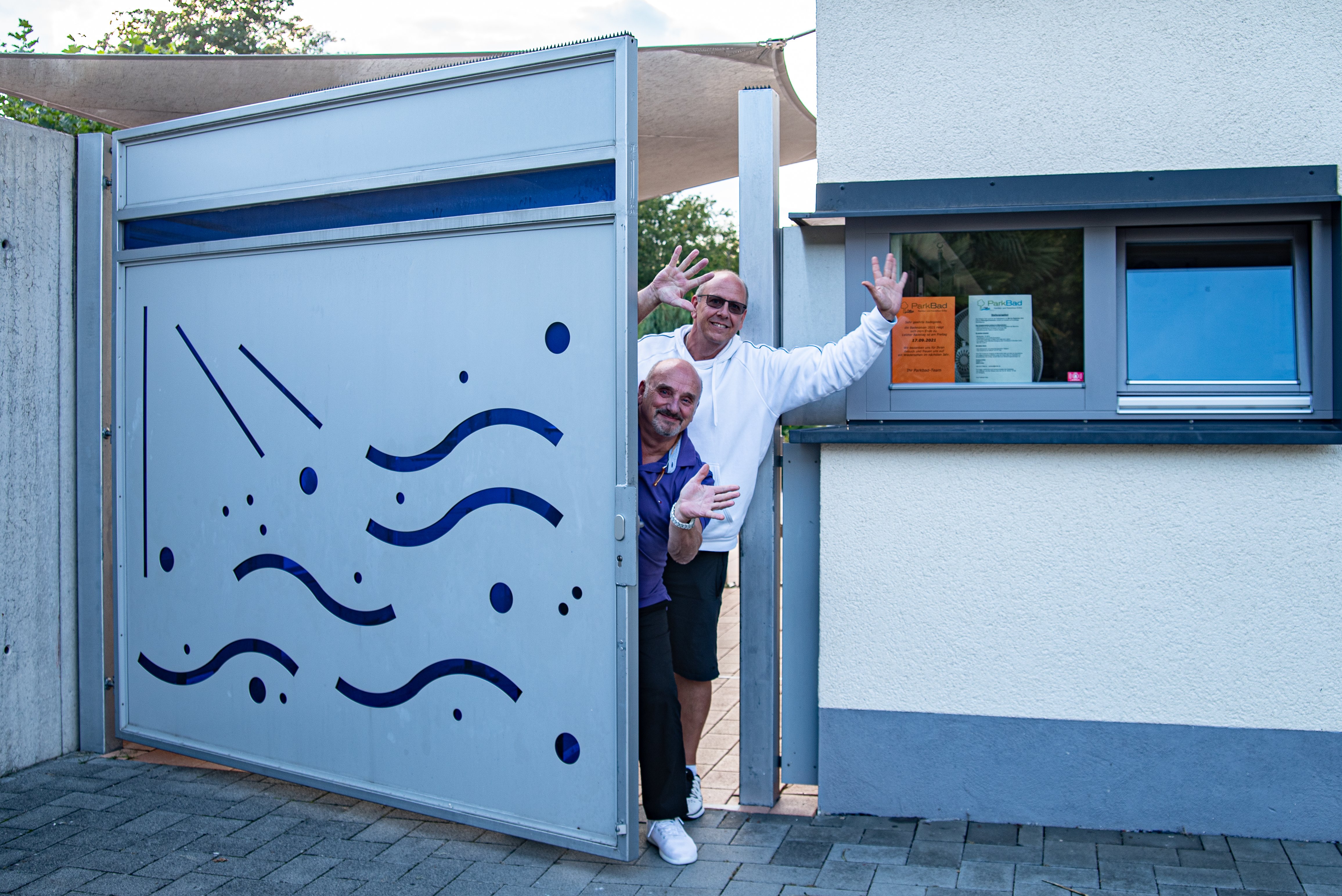 Zwei Männer des Teams winken aus der Tür.