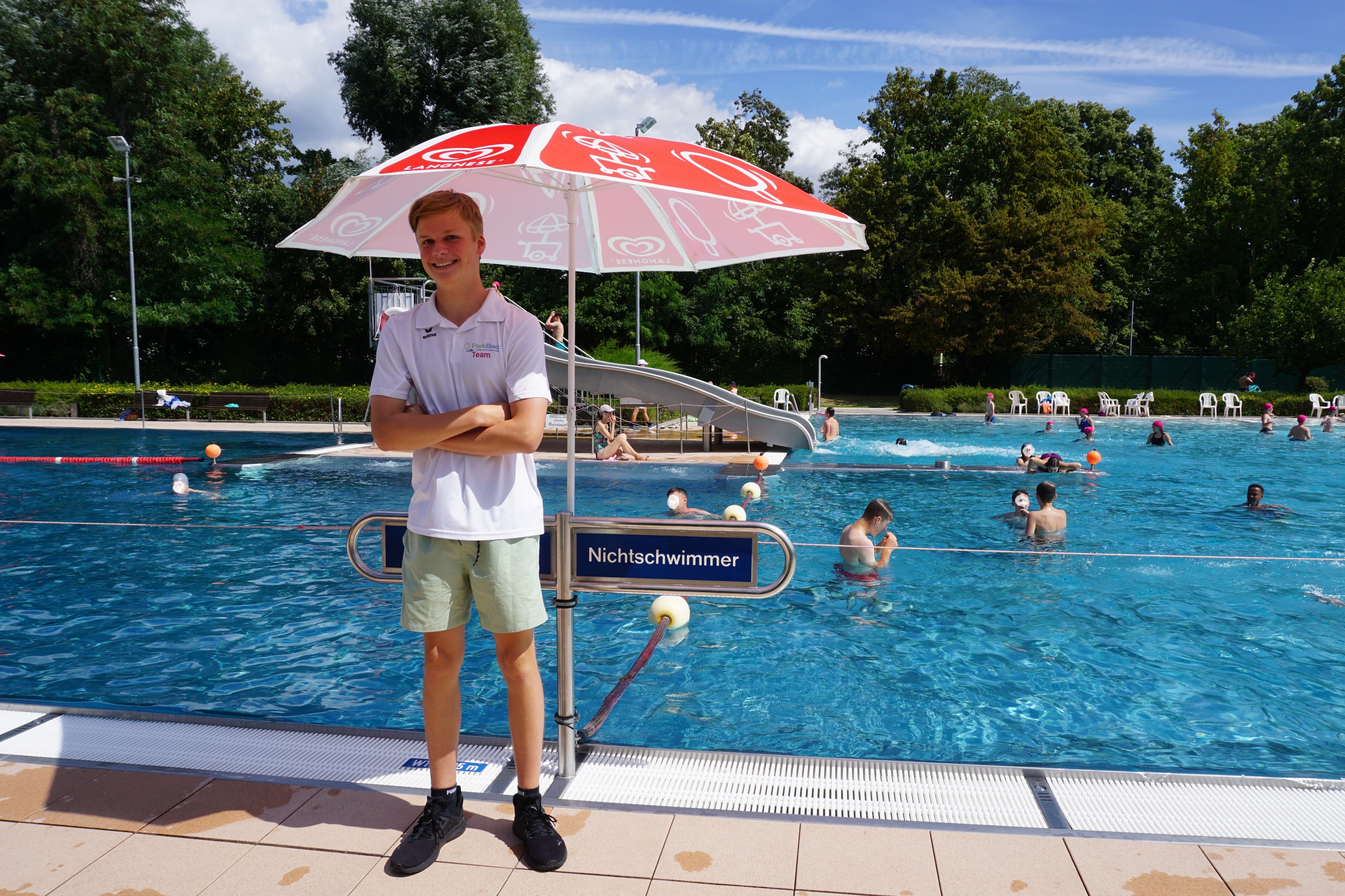 Der Schülerpraktikant unterm Sonnenschirm am Beckenrand.