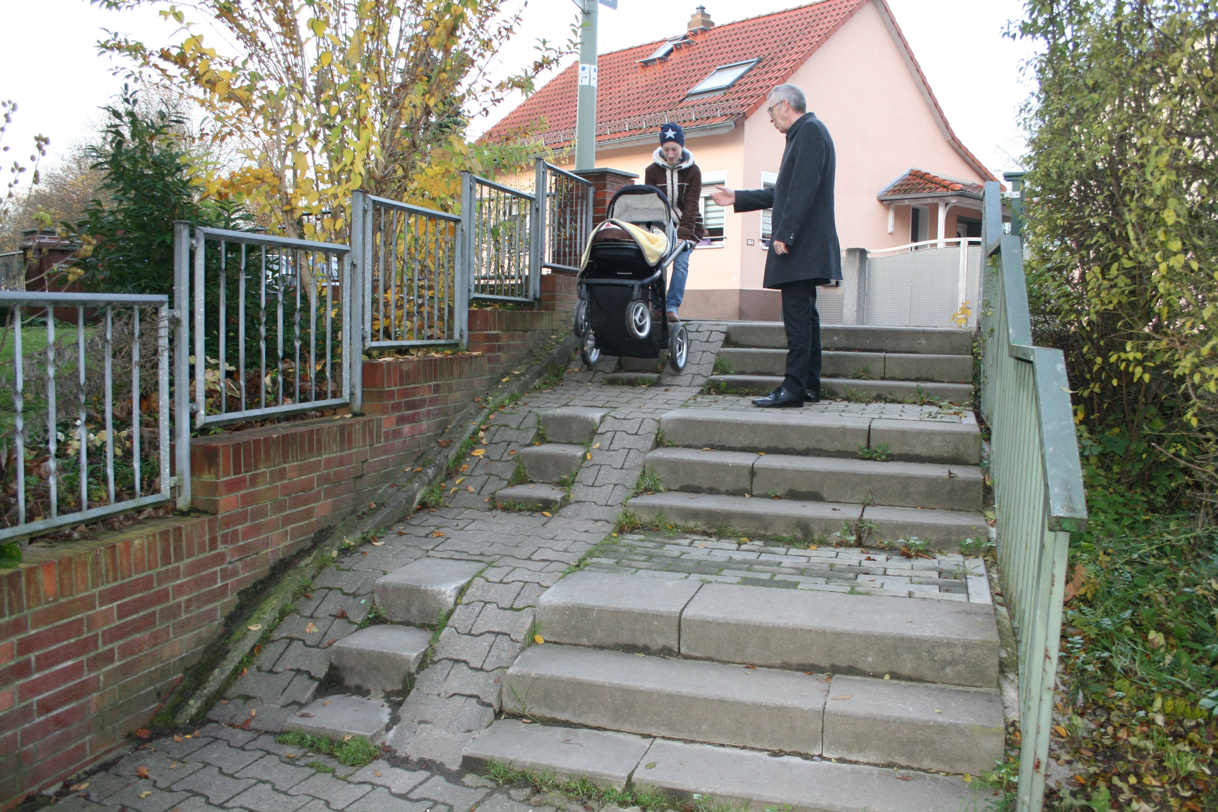 Eine Frau mit Kinderwagen hat Schwierigkeiten, die Treppenstufen am Hattersheimer Weg zu überwinden.