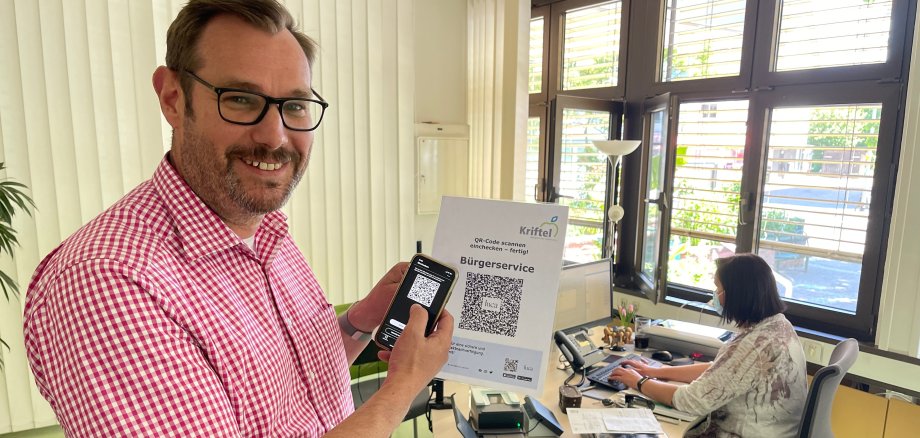 Bürgermeister mit Smartphone und einem Schild mit QR-Code.