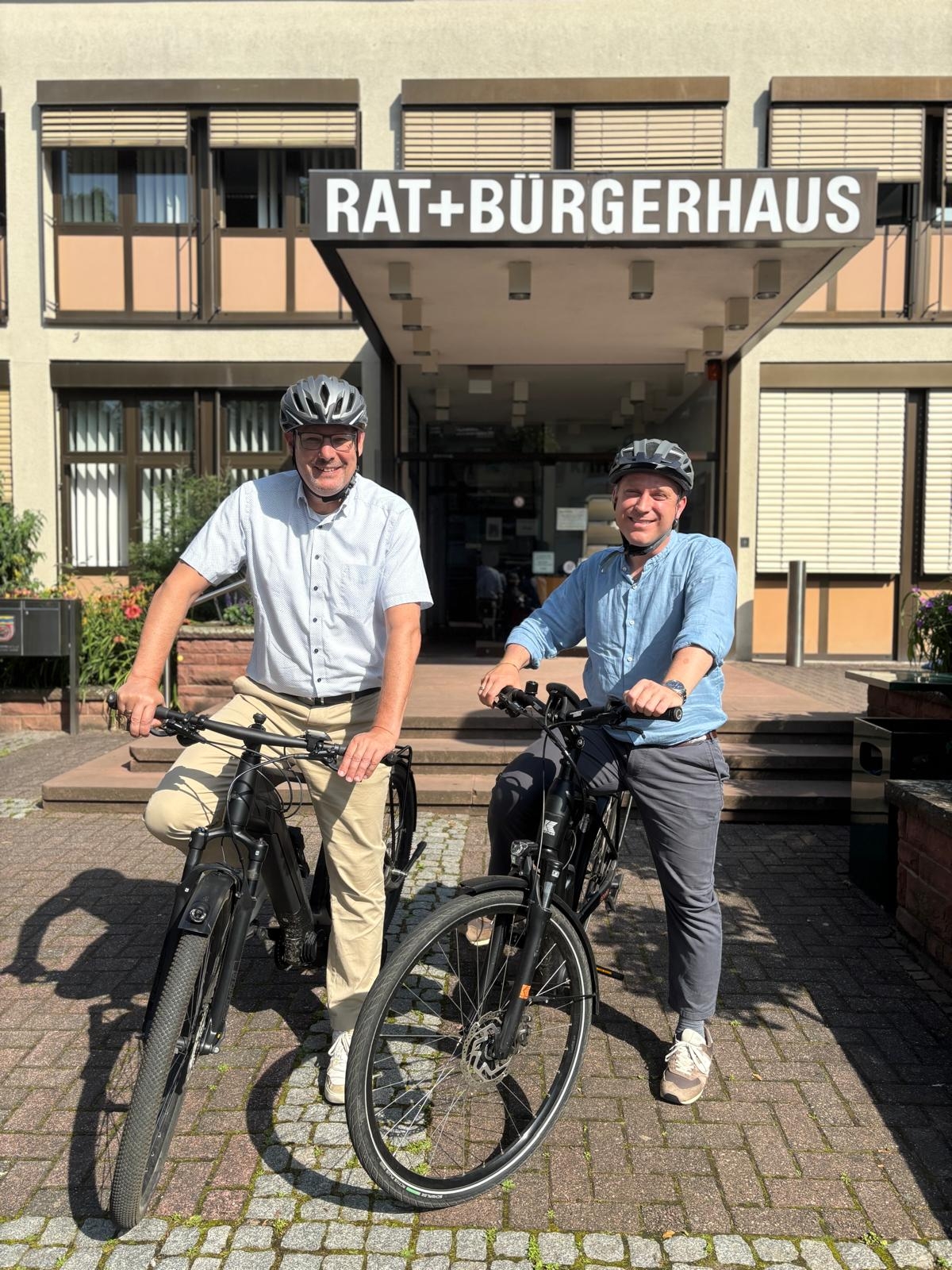 Seitz und Mohr auf dem Fahrrad vor dem Rathaus.