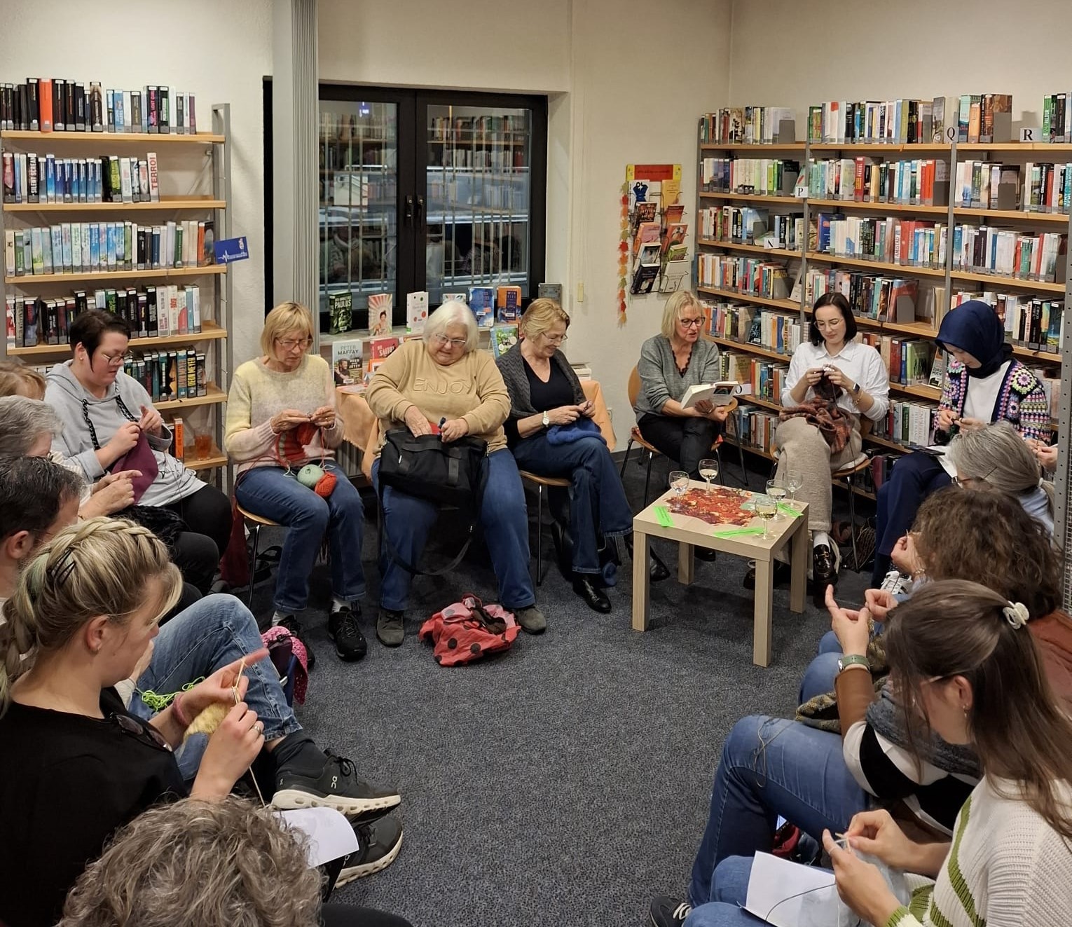 Damen stricken zwischen Bücherregalen.