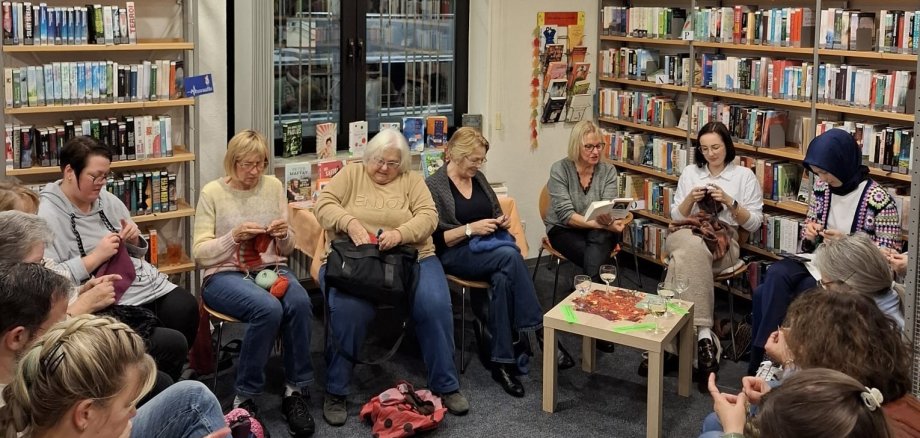 Damen stricken zwischen Bücherregalen.