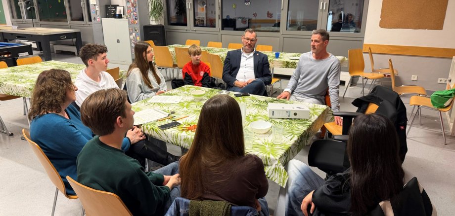 Jugendliche mit Erwachsenen an einem Tisch.