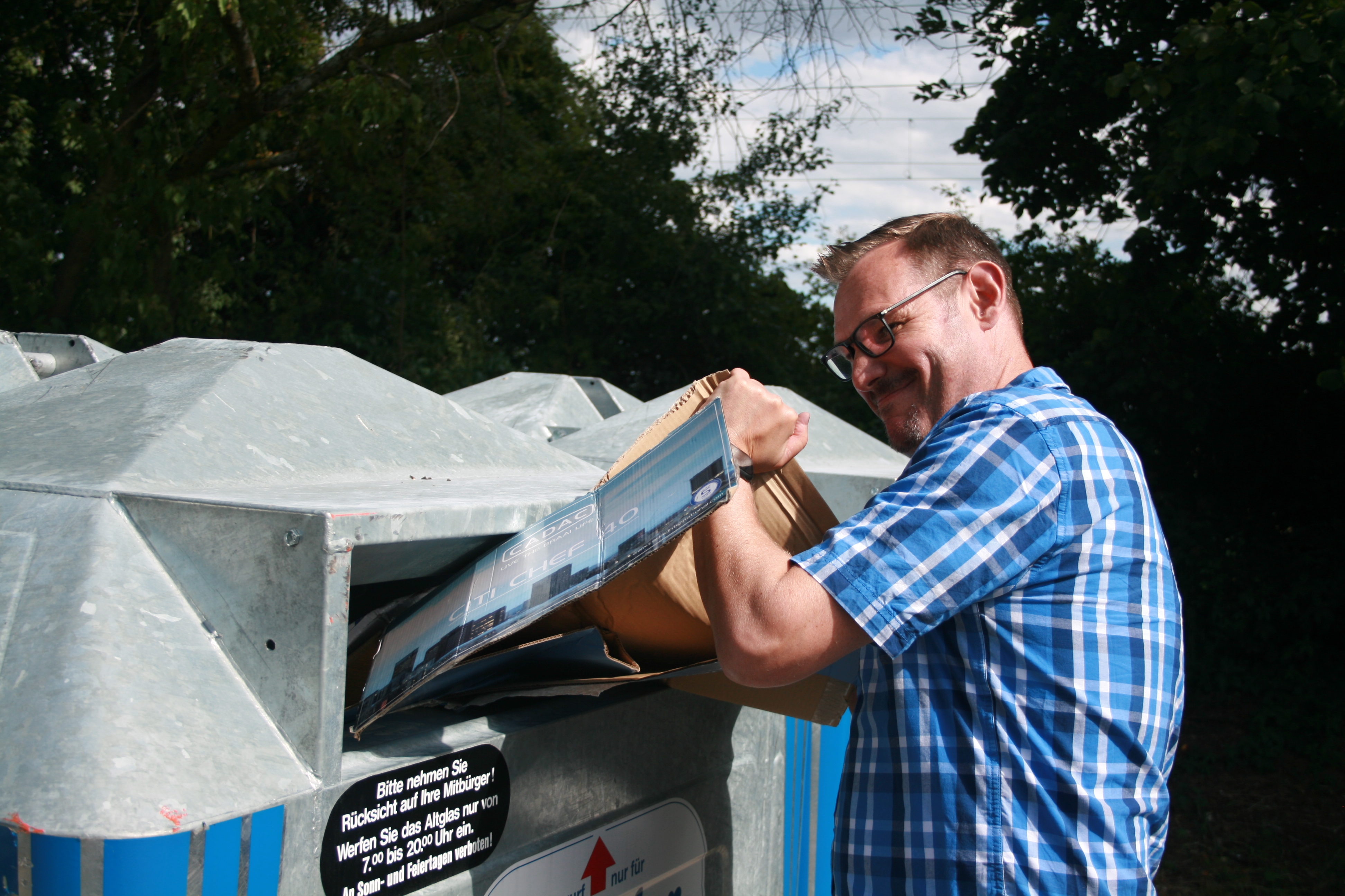 Bürgermeister Seitz versucht einen Karton in einen vollen Papiercontainer zu pressen.
