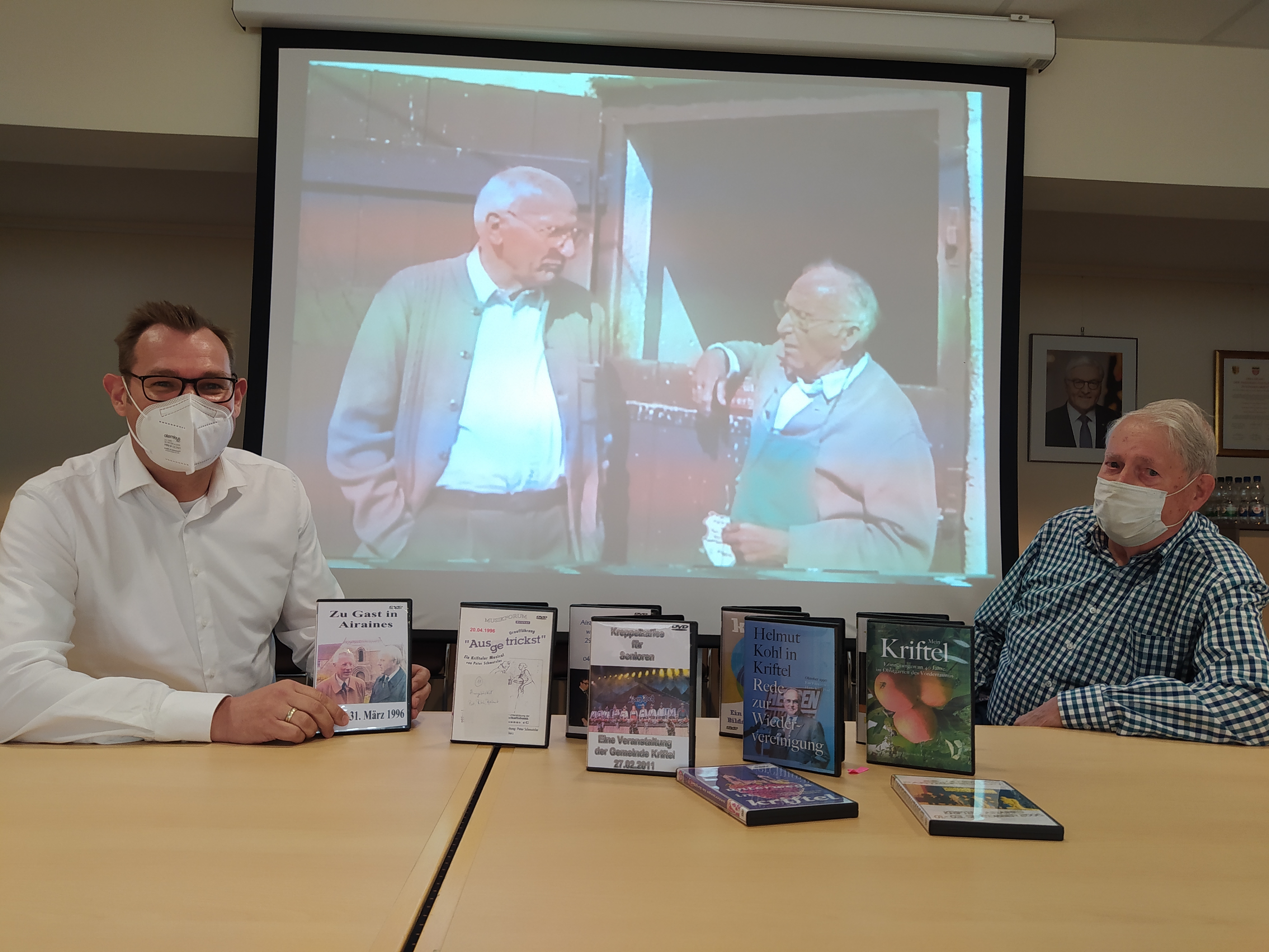 Bürgermeister Seitz und Hans-Karl Post sitzen vor einer Leinwand. Darauf sieht man einen Filmausschnitt.