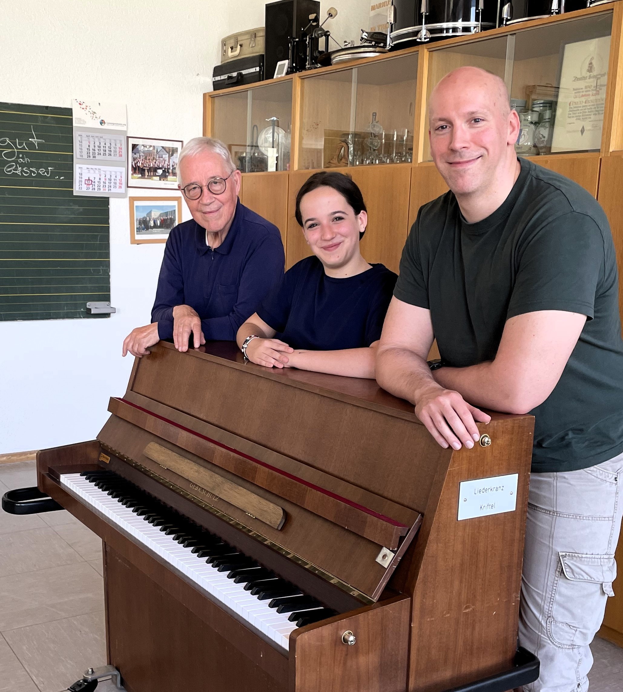 Miray hinter einem Klavier mit Lehrer und Vater.