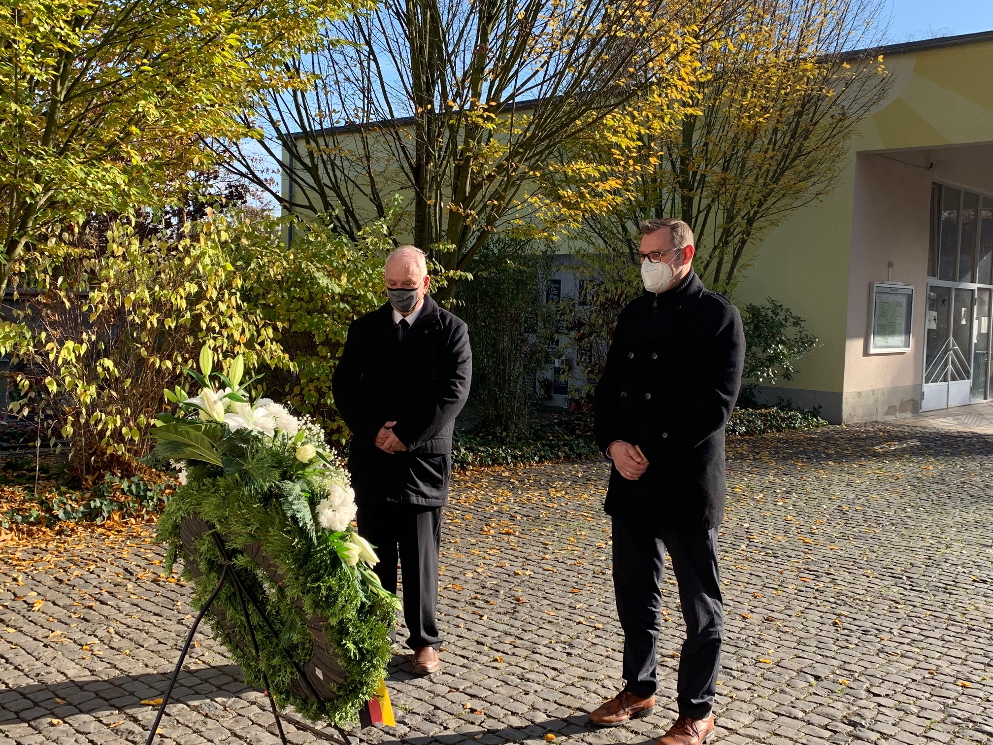 Bürgermeister Seitz und Bodo Knopf, Vorsitzender der Gemeindevertretung, vor einem Kranz auf dem Friedhof.