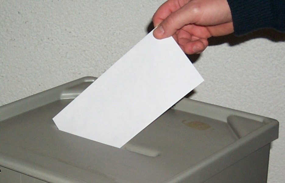 Eine Hand wirft einen Stimmzettel in die Wahlurne.