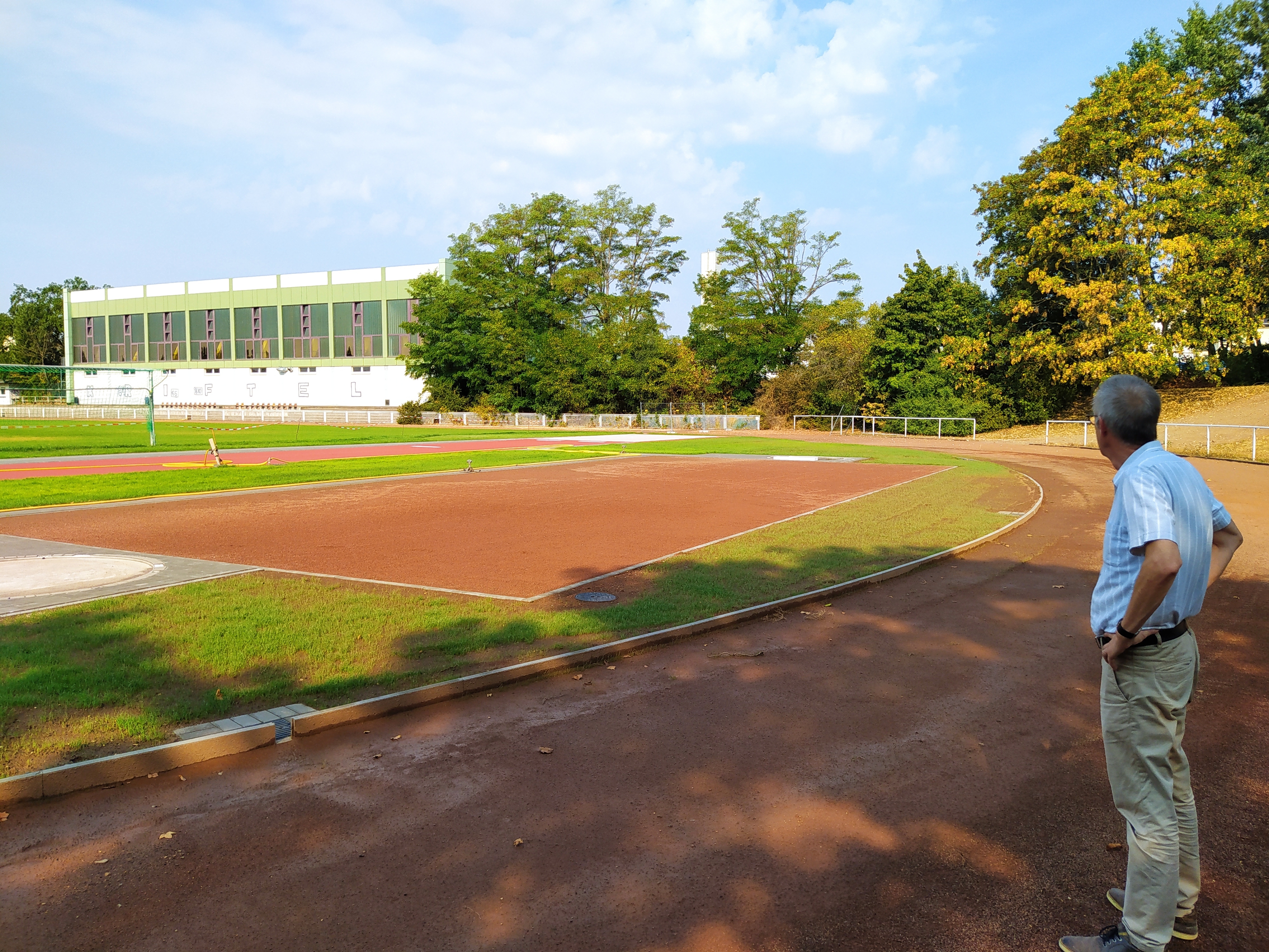 Man sieht im Vordergrund die neue Weitsprung- und Kugelstoßanlage, im Hintergrund das grüne Fußballfeld.