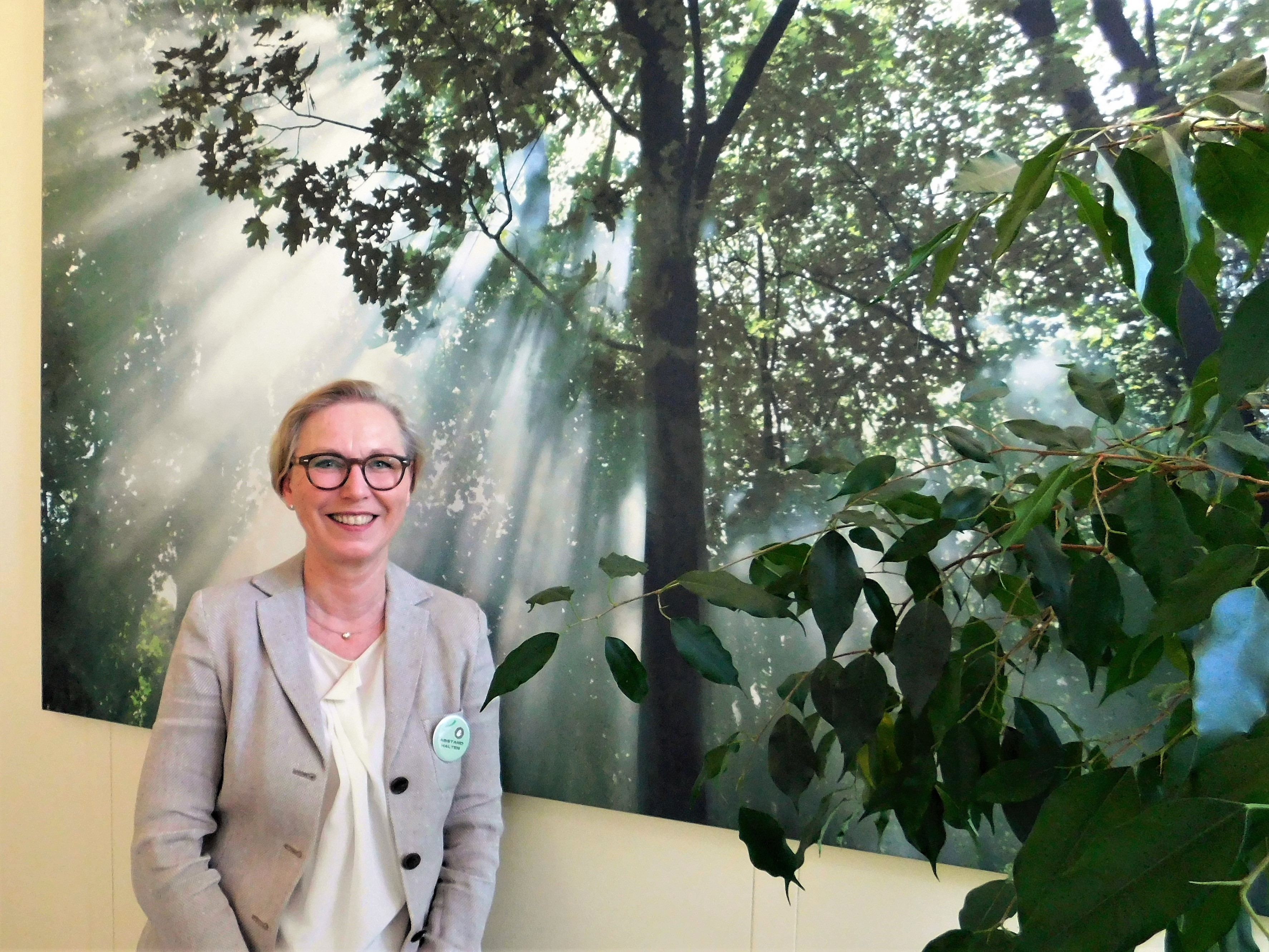 Elke Wetterau-Bein vor ihrem riesigen Lieblingsfoto im Büro: Ein Baum ist zu sehen, durch den sich Lichtstrahlen brechen.