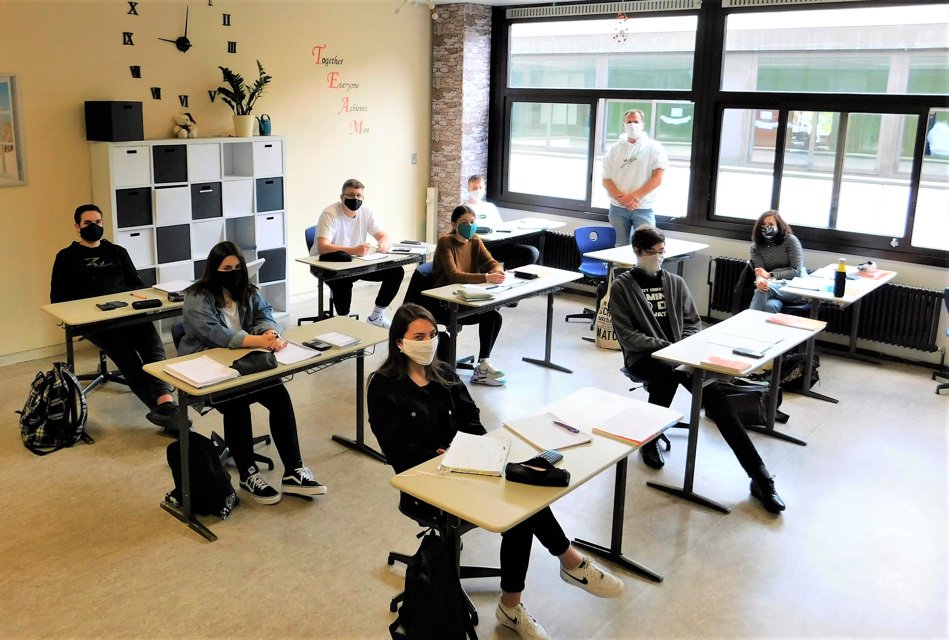 JUgendliche mit Masken sitzen, jeweils alleine an einem Tisch, im Klassenraum.