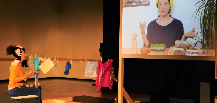 Die Schauspielerin neben einer Wäscheleine und einem großen Bildschirm.