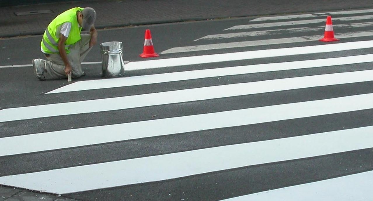 Ein Arbeiter malt einen Zebrastreifen auf die Straße.