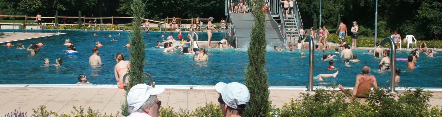 Zwei Senioren vor dem belebten Schwimmbecken des Parkbads