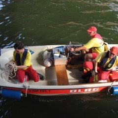 Aufsicht auf ein Rettungsboot mit drei Insassen in Kleidung der DLRG beim Anlegen an den Steg