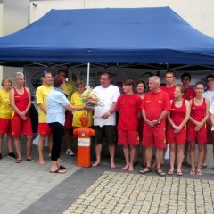 Eine Gruppe von Freiwilligen der DLRG bei der Überreichung eines Blumenstraußes vor einem Pavillon der DLRG