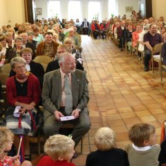 Ein vollbesetzter Kircheninnenraum bei einem Gottesdienst, auf den vorderen Stufen sitzen Kinder