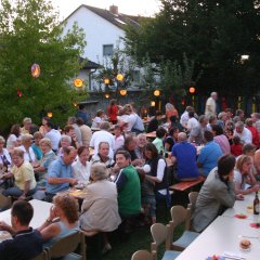 Viele Menschen auf Bierbänken im Kirchgarten beim Sommerfest, in den Bäumen hängen Lampions