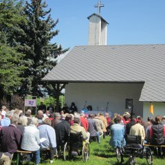 Gemeinde auf Bänken im Freien vor der Bonifatiuskapelle während eines Gottesdienstes
