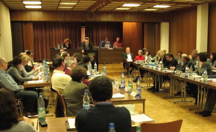 Eine Sitzung im Saal. Viele Politiker/innen sitzen an Tischen im Rathaus.