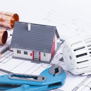 Sanitärinstallation
Baupläne, Heizungsrohre, Werkzeuge und ein Miniaturhaus auf einem Tisch
