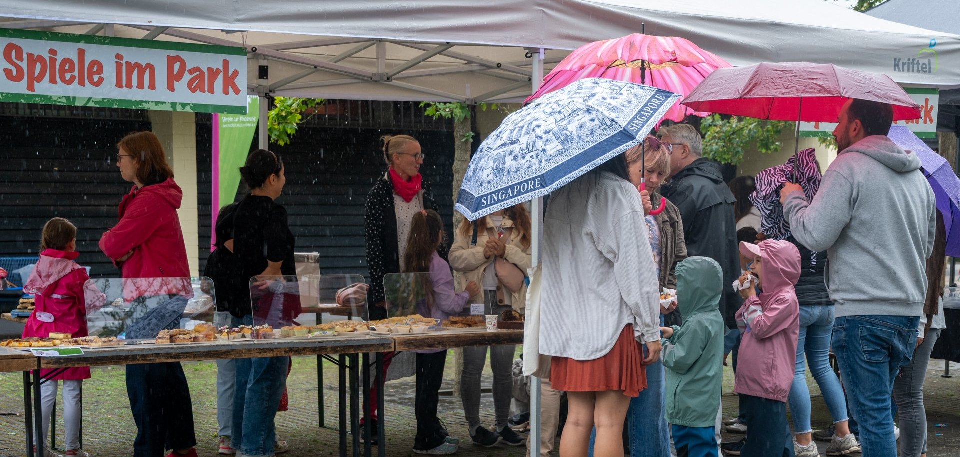 Besucher am Kuchenstand mit Schirmen.