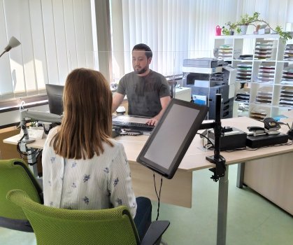 Eine Bürgerin sitzt vor dem Schreibtisch eines Bürgerservice-Mitarbeiters.