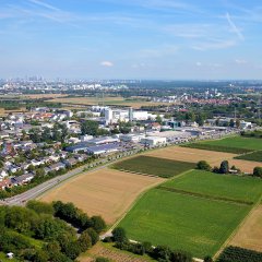 Kriftel aus der Vogelperspektive: Vorne erstreckt sich das Hochfeld, in der Mitte Gewerbe und Wohngebiet Kriftels und im Hintergrund ist die Skyline Frankfurts zu sehen.